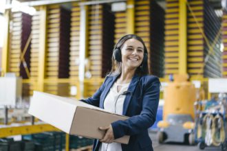 Young woman working at parcel service, carrying parcel in warehouse